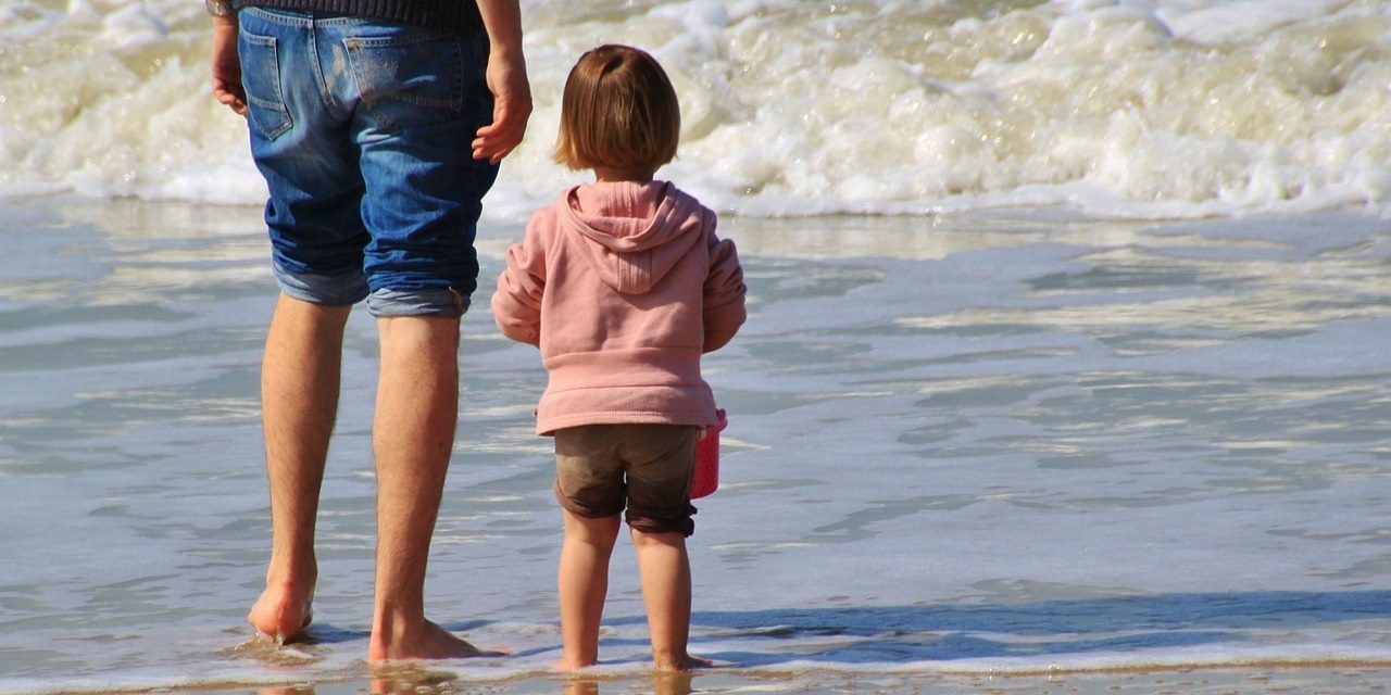 Ein Kind und ein Erwachsener schauen aufs Meer.
