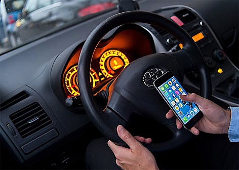 Ein Mann sitzt in einem Auto am Steuer und hält ein Smartphone in der Hand