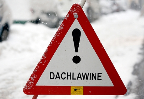 Ein Warnschild mit der Aufschrift "Dachlawine" im Schnee