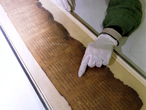 Eine Forscherin mit weißen Handschuhen deutet auf eine Stelle in einer der Schriftrollen von Qumran