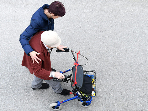 Eine Frau stützt eine alte Frau mit Rollator