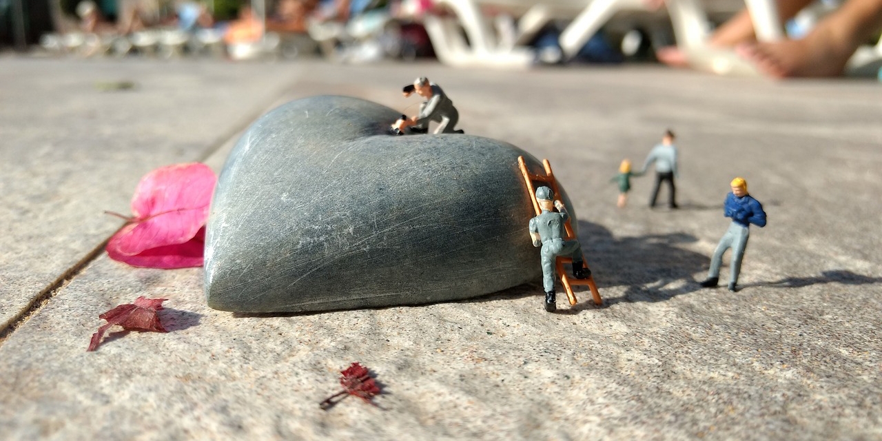 Kleine Miniaturmenschen bearbeiten ein Steinherz