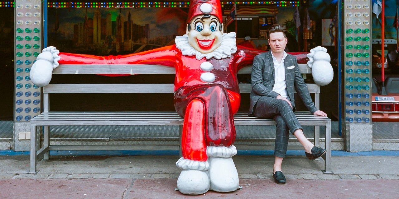 Konstantin Gropper sitzt nemebn einem Clown im Wiener Prater