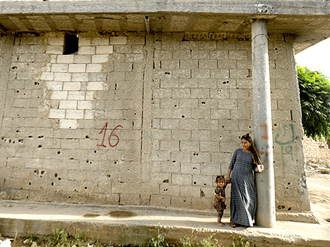 Eine Frau mit einem Kleinkind vor einem zerstörten Gebäude in Kobane, Syrien