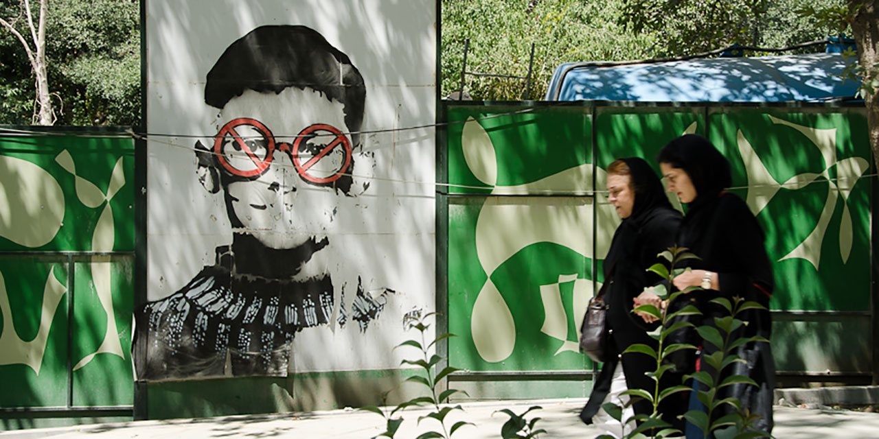 Straßenszene im Iran: Zwei Frauen gehen an einem Graffiti vorbei, das einen Buben zeigt mit Verbotszeichen vor den Augen