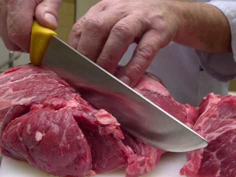 Ein Mann schneidet mit einem Messer rohes Fleisch