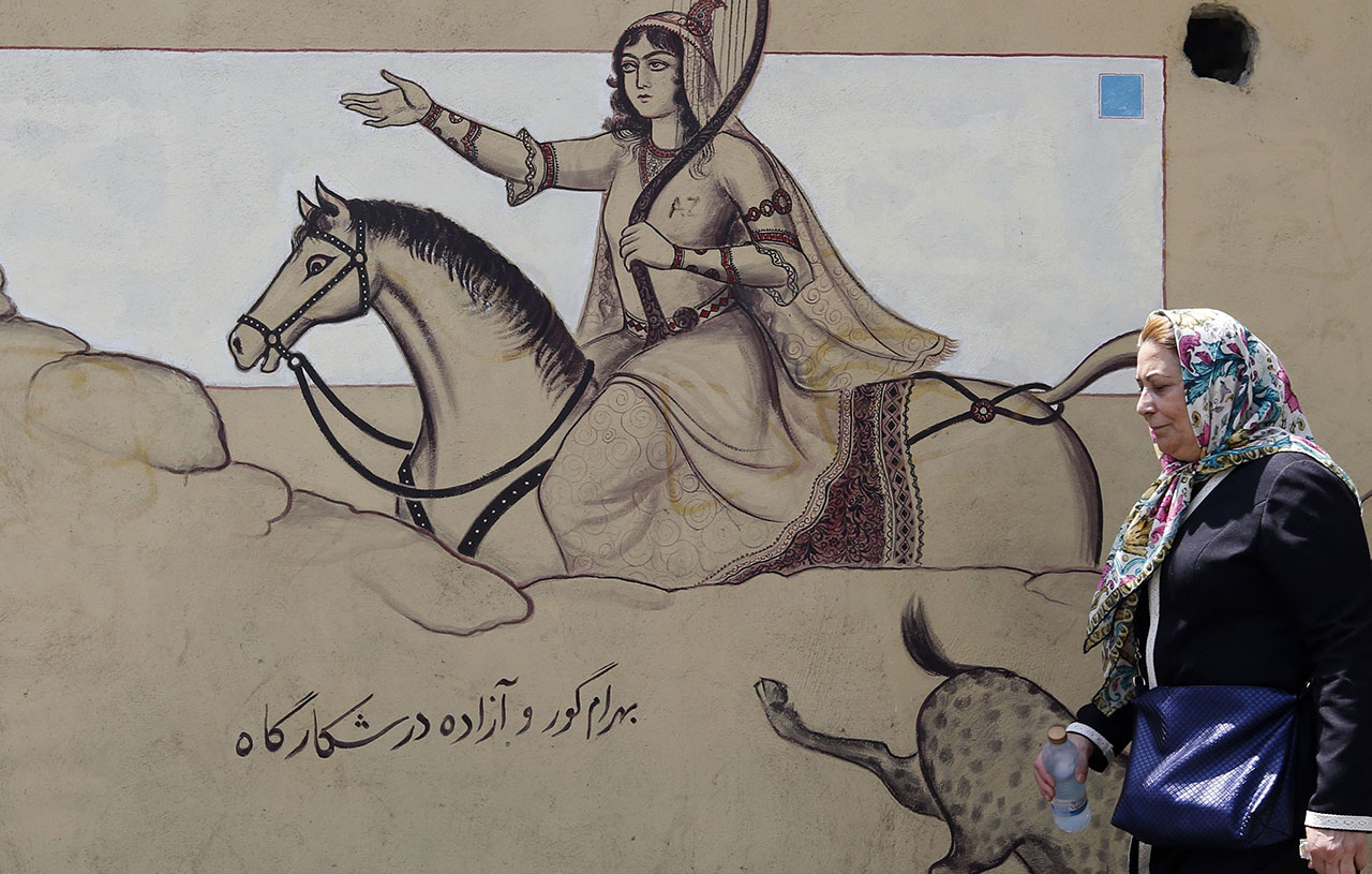 An Iranian woman walks past a mural painting illustrating ancient Persian poetry in the Iranian capital Tehran on August 7, 2018