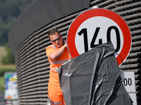 Ein Arbeiter stellt ein Tempo 140-Schild auf