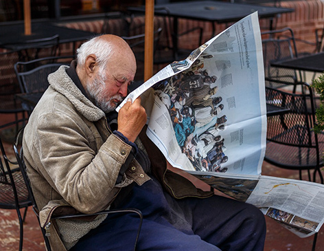 Ein amerikanischer alter Mann sitzt und liest Zeitung und sieht dabei aus, als würde er eingeschlafen sein