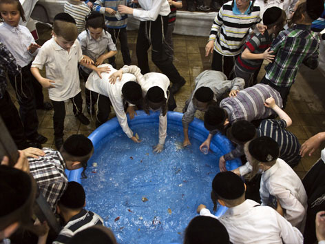Orthodoxe jüdische Buben spielen bei einem blauen Planschbecken mit den darin schwimmenden Fischen