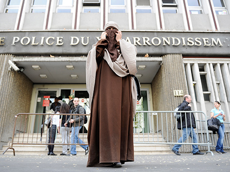 Eine Frau in Ganzkörperverschleierung steht vor einer Pariser Polizeistation