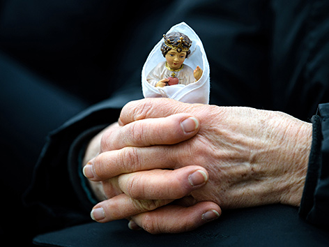 Eine alte Frau hält eine kleine Marienfigur in den gefalteten Händen