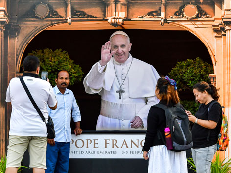 Asiatische Gläubige in den Vereinigten Arabischen Emiraten vor einem Plakat von Papst Franziskus