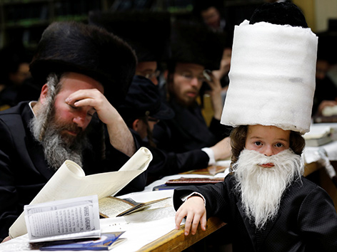 Ein Rabbi liest aus dem Buch Esther, daneben ein verkleideter Bub