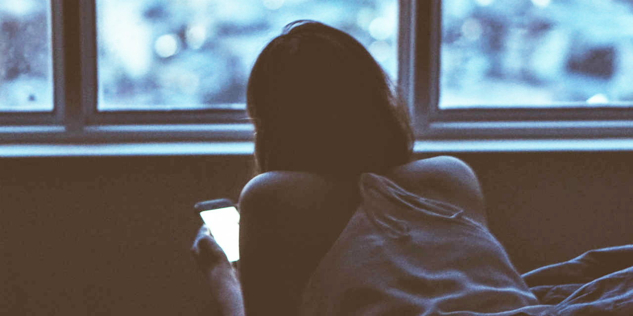Eine Frau liegt mit Handy auf dem Bett