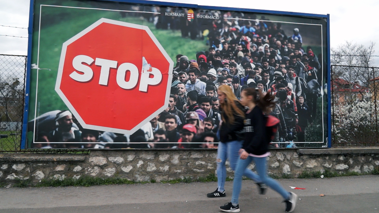 Zwei Mädchen gehen an einem großen Plakat vorbei, das gegen Zuwanderung hetzt.