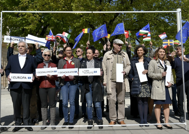 Die Liste 1 Europa bei ihrer Plakatpräsentation. Unterstützerinnen und Unterstützer stellen sich in einen Metallrahmen