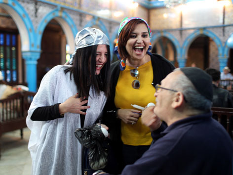 Zwei muslimische Frauen lachen mit einem Rabbiner in der tunesischen Synagoge Ghriba.