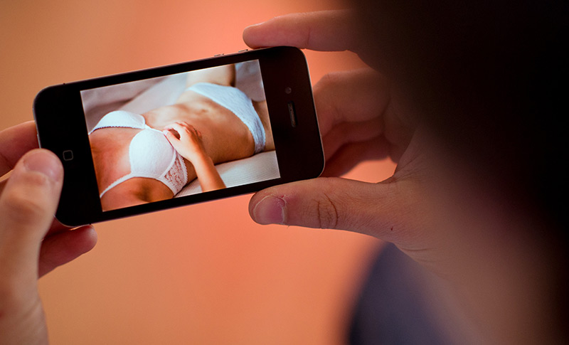 Frau in Unterwäsche: Ein junger Mann betrachtet ein erotisches Bild auf seinem Handy