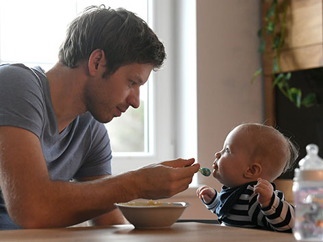Ein Mann füttert ein kleines Kind mit dem Löffel