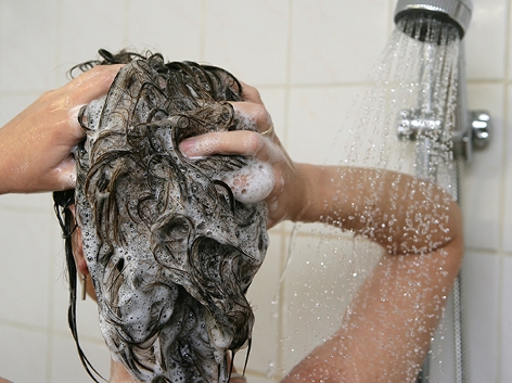 Frau unter der Dusche mit Schaum im Haar, von hinten fotografiert.