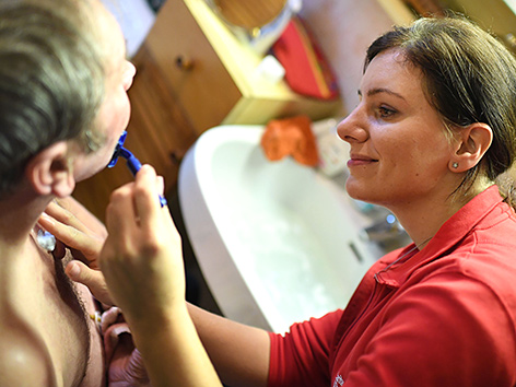 Eine Frau rasiert einen pflegebedürftigen Mann