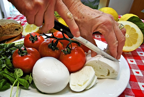 Frau schneidet Mozzarella auf einem Teller mit Paradeiser und Basilikum
