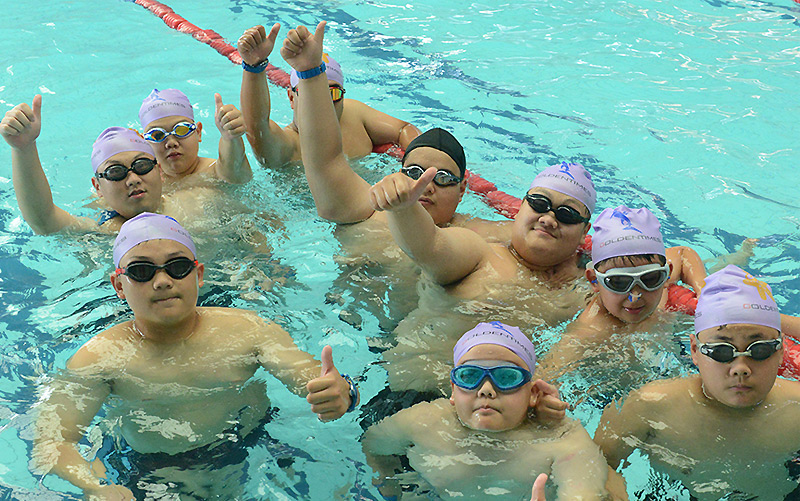 Mehrere dicke Chinesen zeigen in einem Schwimmbecken den Daumen nach oben