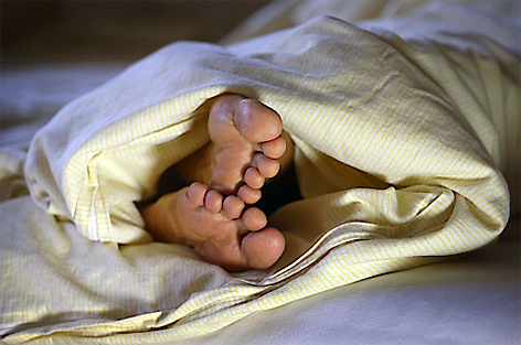 Füße ragen unter einer Bettdecke hervor