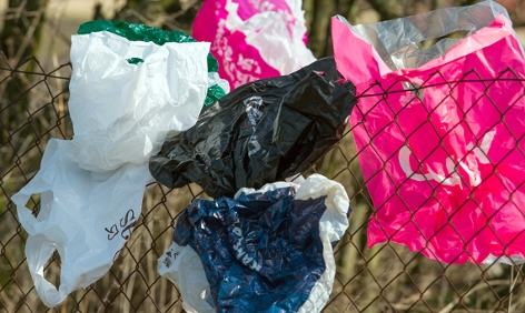 Weggeworfene Plastiksackerl hängen in einem Zaun