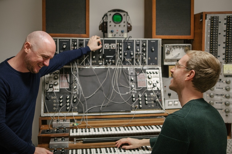 Die Musiker Dorian Concept und Zanshin stehen neben einem Max Brand Synthesizer