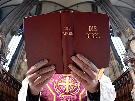 Ein Priester hält eine aufgeschlagene Bibel in den Händen