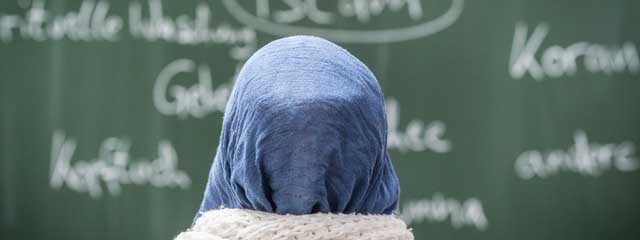 Eine Schülerin mit Kopftuch sitzt in einer Schule bei einer Unterrichtsstunde zum Thema Islam vor einer Tafel