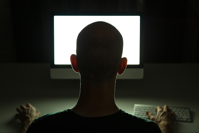 Dunkler Raum: Mann sitzt vor einem Computerbildschirm
