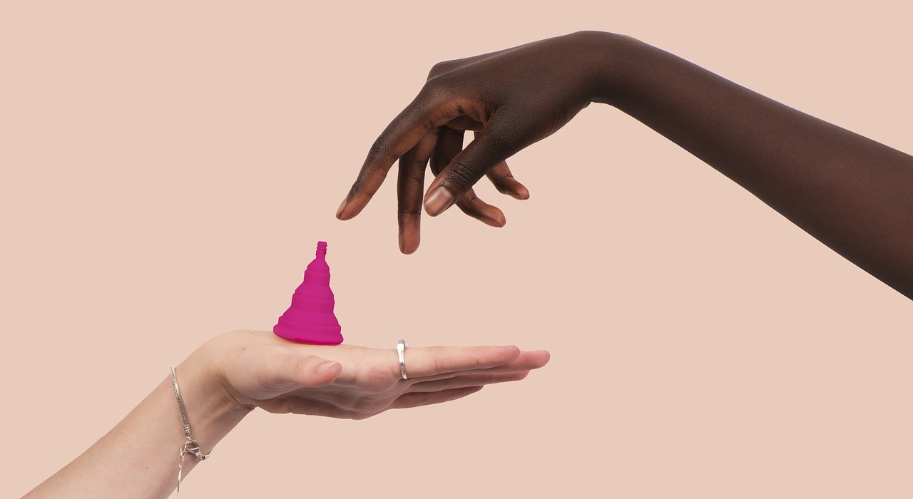 zwei Hände und ein Menstruationscup vor rosafarbenem Hintergrund