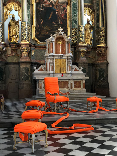 Ein Sessel mit roten Feuerwehrschläuchen umwickelt. Fastenzeit-Installation von Franz Konrad in der Kirche St. Andrä in Graz.