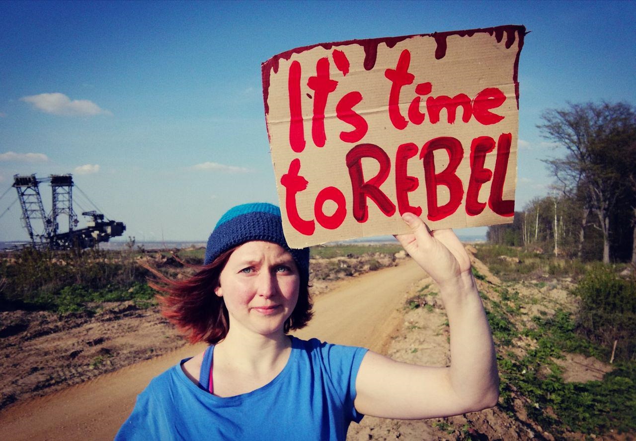 Die "Ende Gelände"-Sprecherin Kathrin Henneberger steht auf einem Feld und hält ein Schild hoch mit der Aufschrift "It's time to rebel"