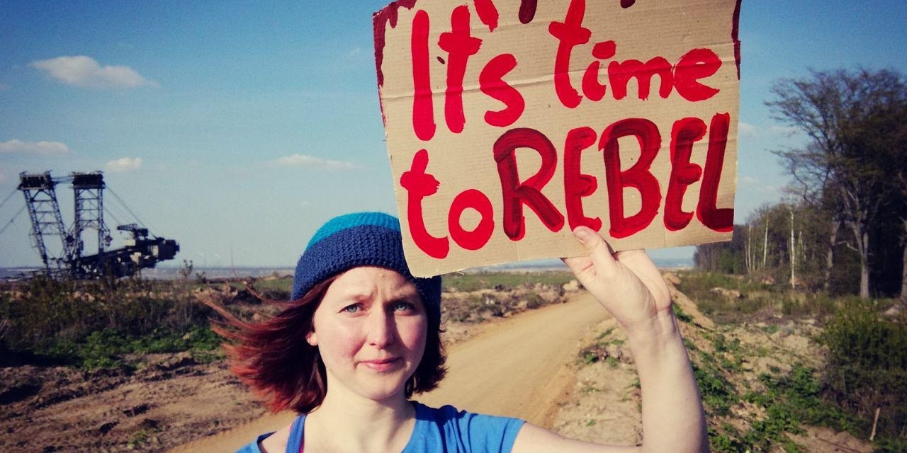Die "Ende Gelände"-Sprecherin Kathrin Henneberger steht auf einem Feld und hält ein Schild hoch mit der Aufschrift "It's time to rebel"