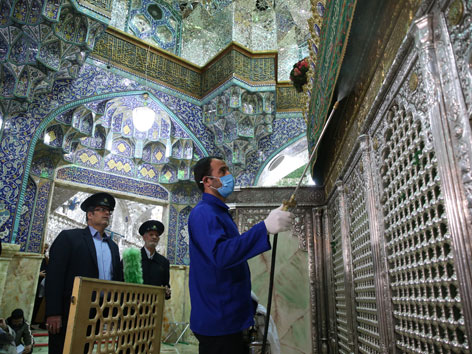 Ein Mann mit Gesichtsmaske desinfiziert das Imam-Reza-Mausoleum im Iran