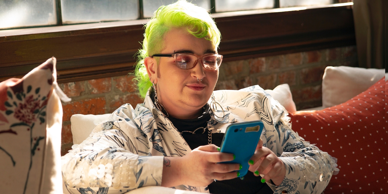 Eine genderqueere Person schaut auf ihr Handy