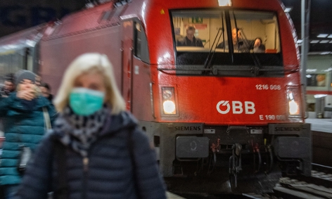Eine Frau mit Atemschutzmaske geht vor einem Zug der ÖBB am Hauptbahnhof in München entlang