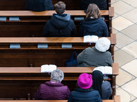 Gottesdienstbesucher sitzen am während der heiligen Messe in der Karmelitenkirche in Straubing (Bayern) in den Bankreihen