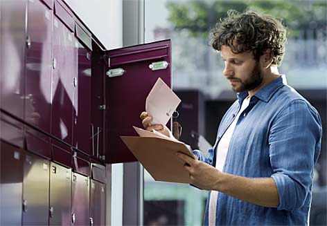 Ein Mann steht vor dem offenen Briefkasten und blättert seine Post durch