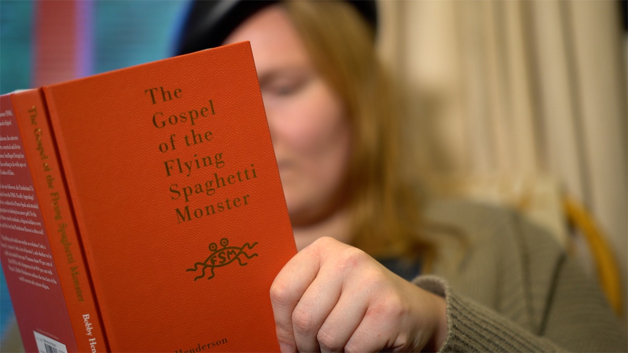 Eine Frau liest die Grundsetze der "Kirche des fliegenden Spaghettimonsters". Filmszene aus "I, Pastafari".