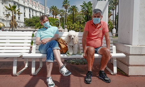 Zwei Urlauber mit Masken sitzen auf einer Bank an der französischen Riviera