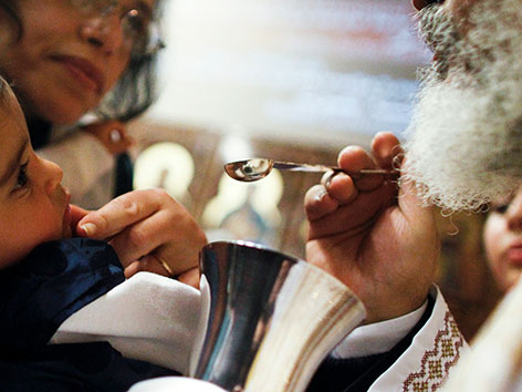 Ein orthodoxer Priester gibt einem Kind  mit einem Löffel die Kommunion