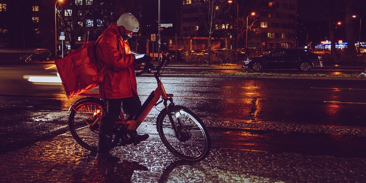 Fahrradkurier in der Nacht, schaut den Weg am Handy nach