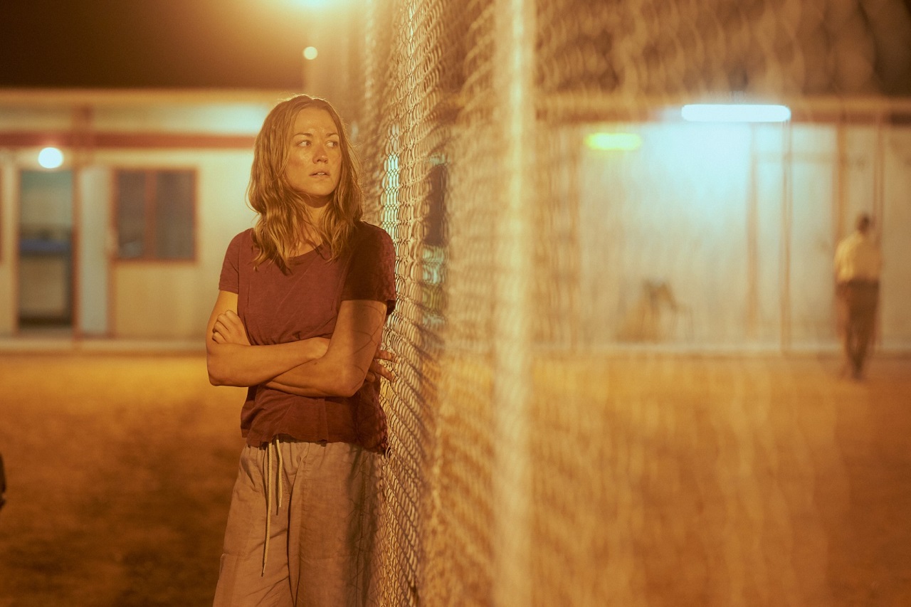 Schauspielerin Yvonne Strahovski als Inhaftierte eines Schubhaftzentrums in der Serie "Stateless", sie steht neben einem hohen Zaun.