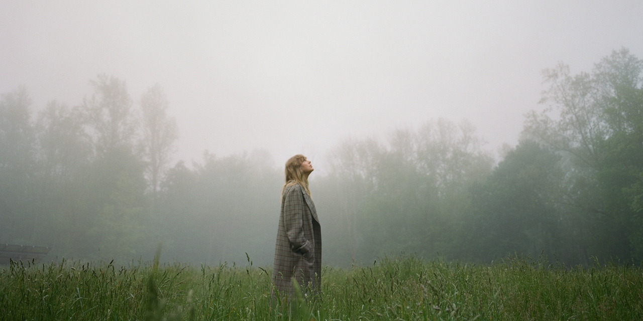 Taylor Swift auf einer Wiese, Nebel verschleiert die Bäume im Hintergrund