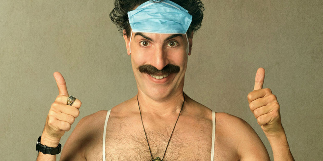 Borat mit Maske auf der Stirn und Daumen hoch
